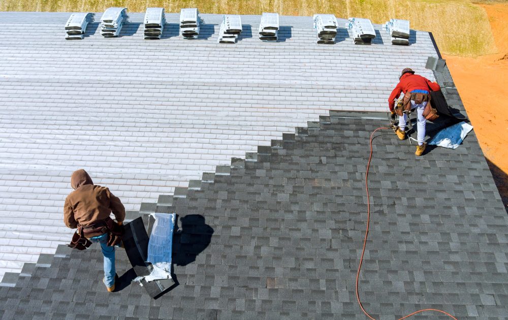 Worker hands installing bitumen roof shingles with air hammer and nail